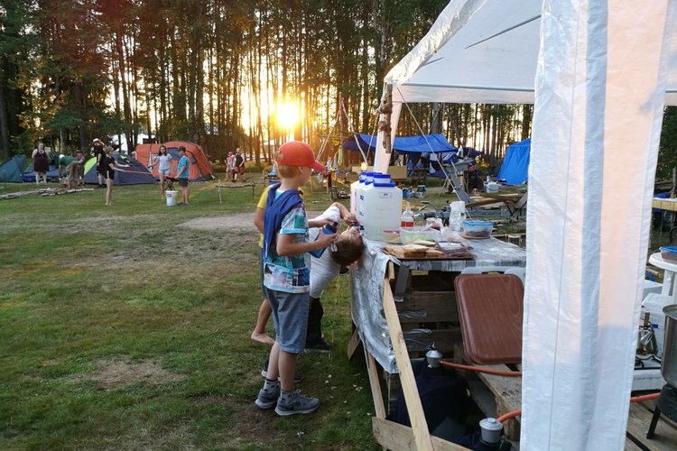 Barn på scoutläger med solen sol går ner bakom träden.